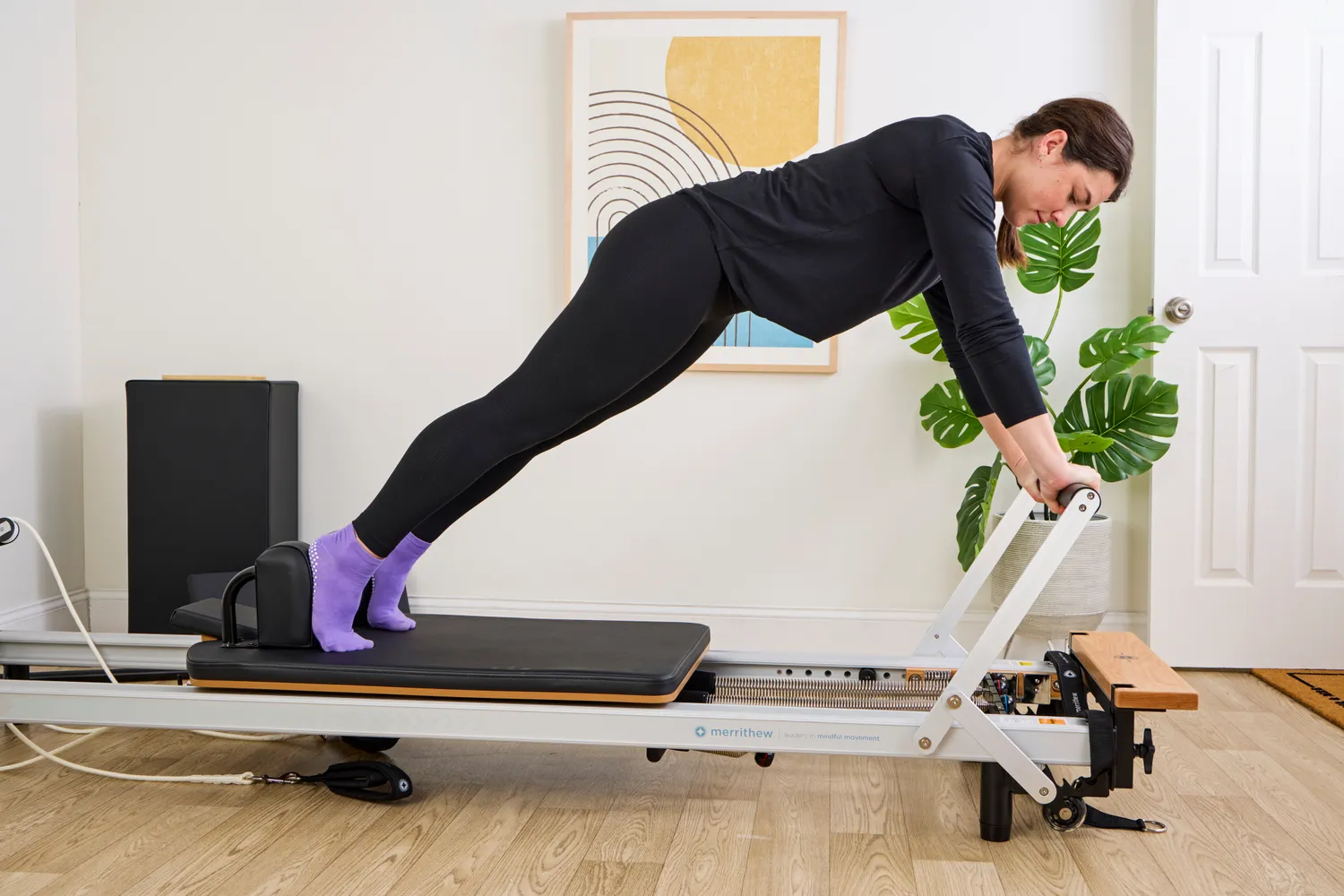 A person performing an exercise on a Pilates reformer in a home setting.