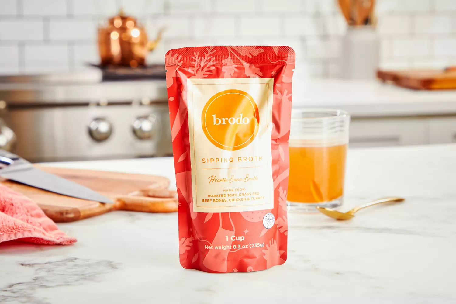 A packet of Brodo Hearth Bone Broth displayed on counter with glass of broth